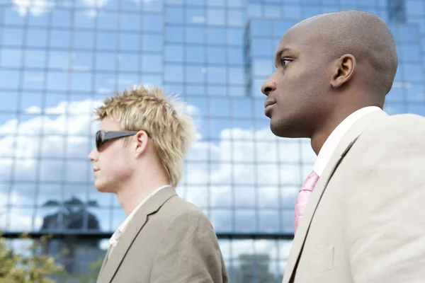 Portrait of two businessmen walking by a modern reflective building. — Stock Photo, Image