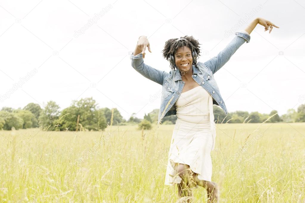 Young black woman dancing in a long grass field while listening to music