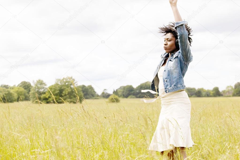 Young black woman dancing in a long grass field whilst listening to music