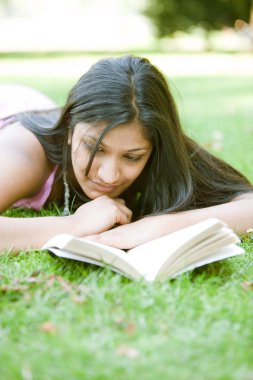 Hintli kız parkta yeşil çim döşeme iken kitap okuma.