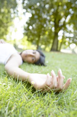 Hintli kız kameraya doğru dinlenme eliyle bir parkta yeşil çimenlerin üzerinde bırakmasını.