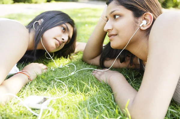 Две индианки делятся своими наушниками, чтобы слушать музыку в парке. . — стоковое фото