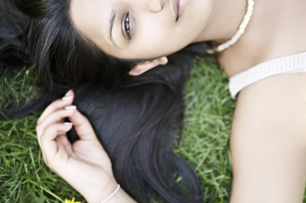 Indian girl's half face laying down on grass — Stock Photo, Image