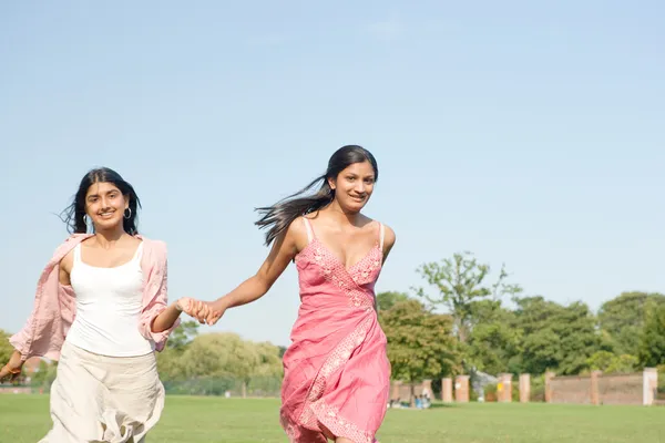 Two Indian girls running in the park while holding hands — Stock Photo, Image