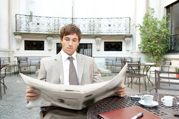 Aantrekkelijke jonge zakenman, de krant lezen terwijl het hebben van een kopje koffie — Stockfoto