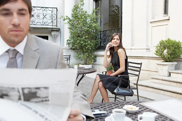 Два дела на террасе классического здания читают газету и разговаривают по мобильному телефону. . — стоковое фото