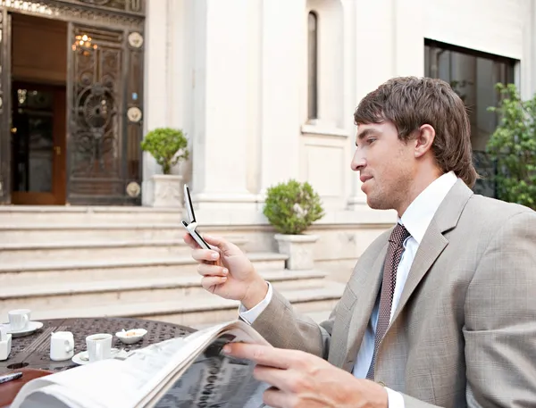 Empresário usando um telefone celular enquanto lia o jornal em um terraço de café — Fotografia de Stock