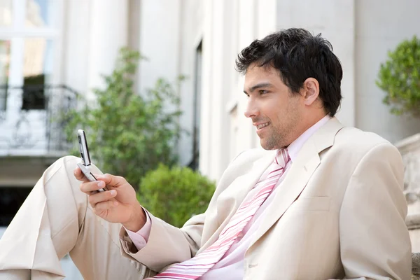 Atractivo hombre de negocios usando su teléfono celular mientras está sentado en los escalones — Foto de Stock