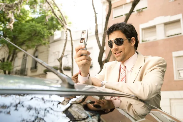 Joven hombre de negocios usando su teléfono celular mientras se apoya en su coche — Foto de Stock