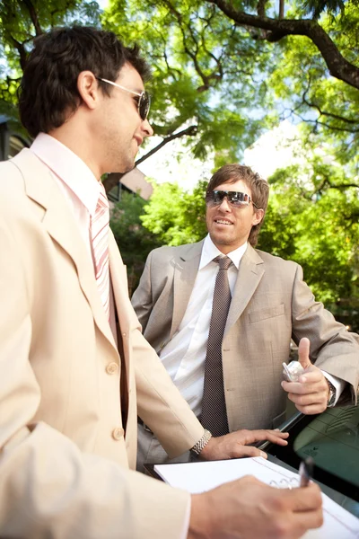 Two businessmen having a conversation while leaning on a car — Stock Photo, Image