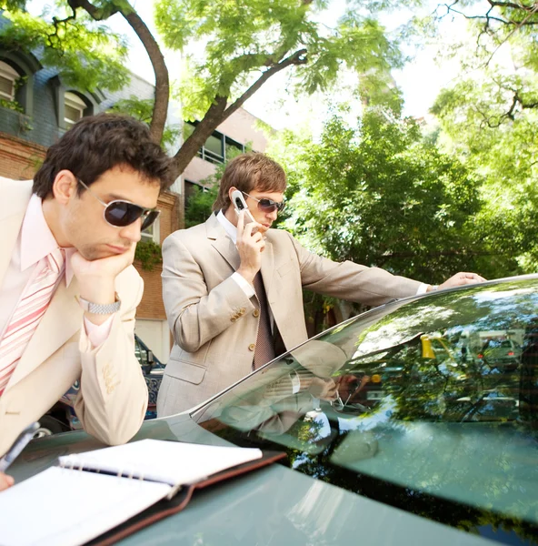 Attraktive Geschäftsleute arbeiten im Freien zusammen, während sie sich auf ein Luxusauto stützen — Stockfoto