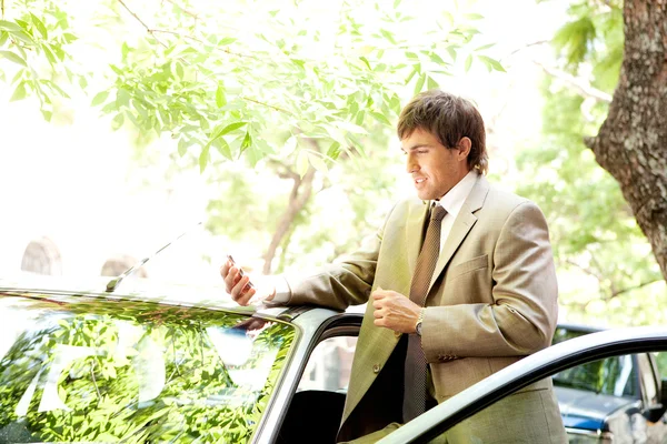 Attractive young businessman using a smart phone while leaning on the door of his car — Stock Photo, Image