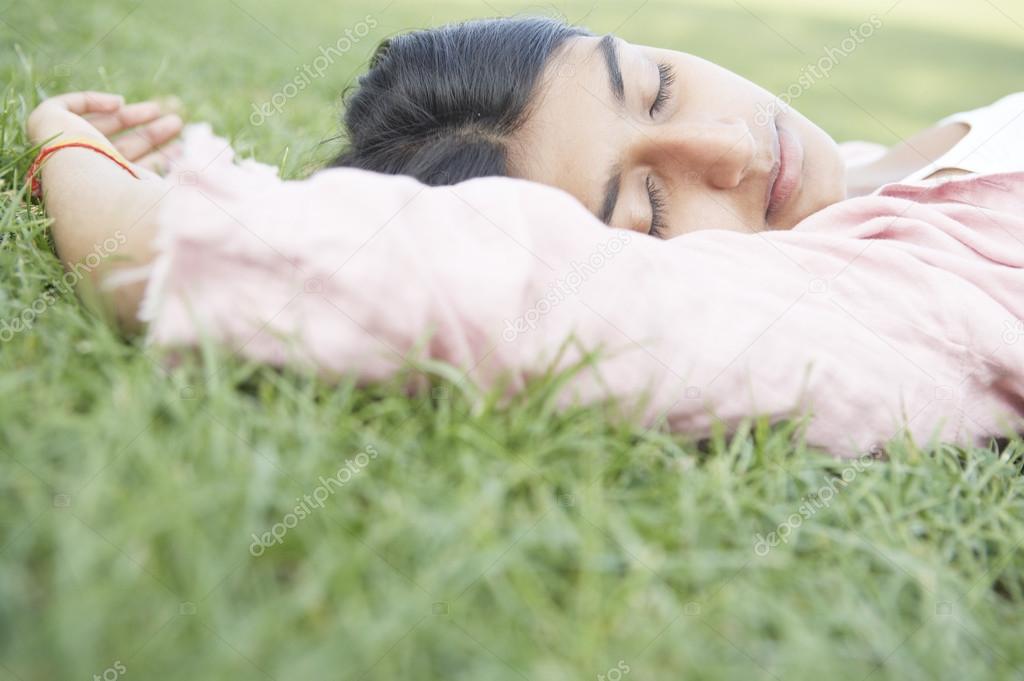 indian girl laying down on green grass with her eyes closed