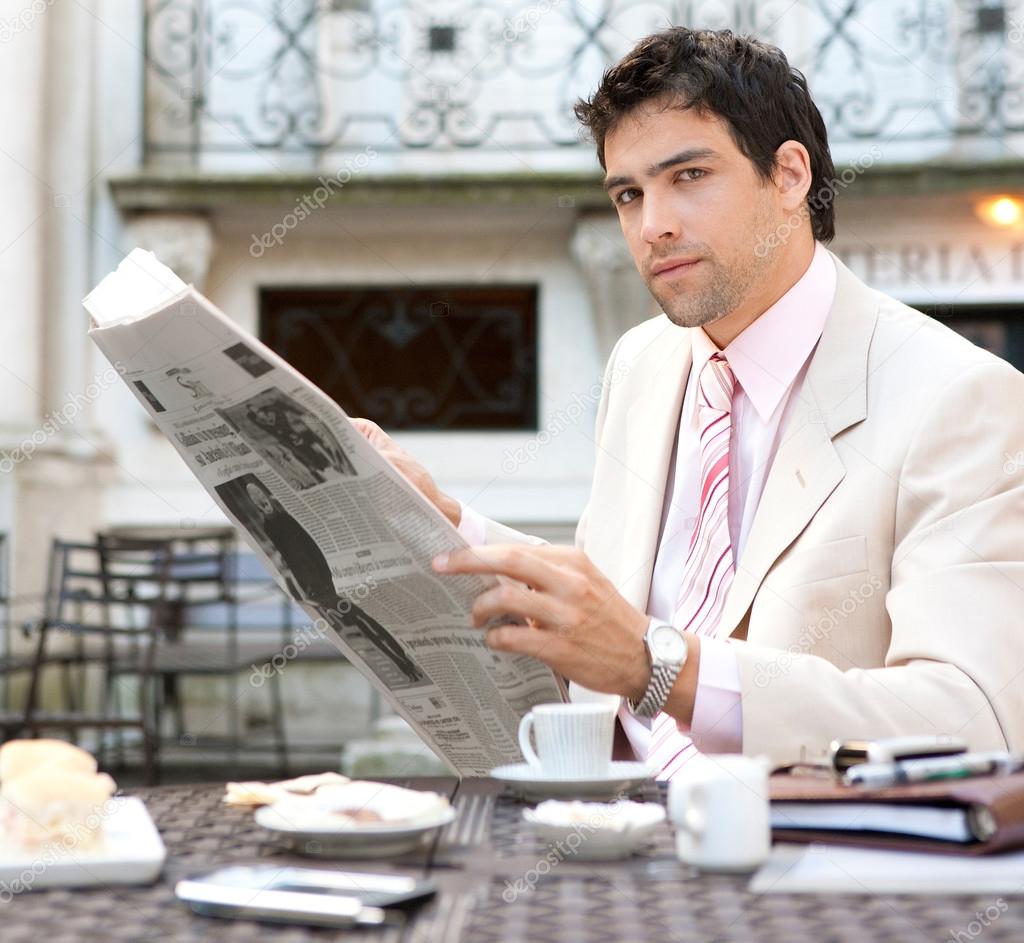 Attractive businessman reading the newspaper while having breakfast