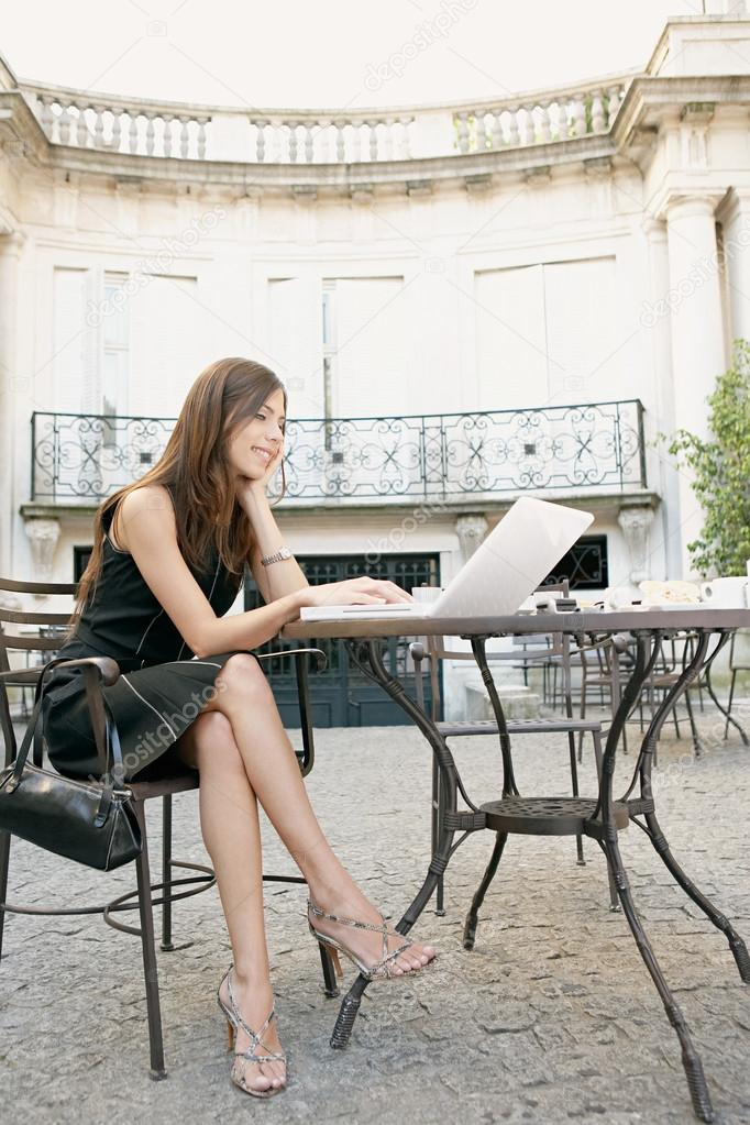 Attractive young businesswoman using a laptop computer while sitting at a coffee shop's terrace table.