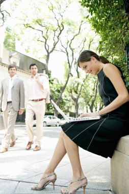 Two businessmen walking in the street and looking at a sexy businesswoman sitting down using her laptop computer. clipart