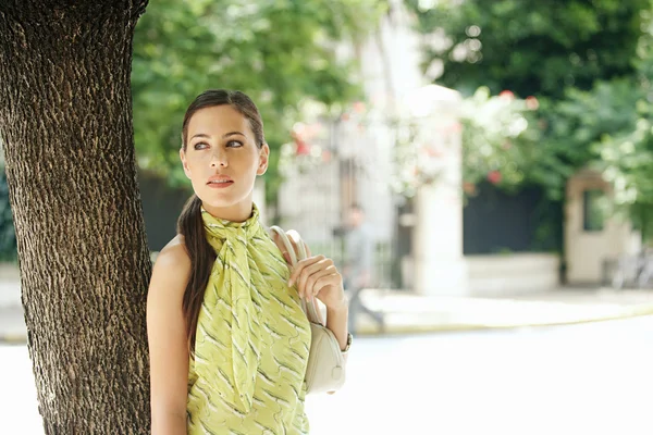 Attractive young businesswoman standing under a tree in the city — Stock Photo, Image