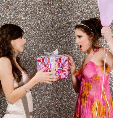 Young woman offering a gift to a birthday girl at a party