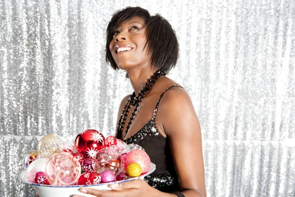 Jovem mulher negra segurando um prato cheio de bolas de Natal — Fotografia de Stock