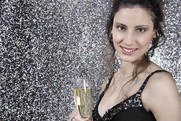 Flicka håller ett glas champagne mot silver glitter bakgrund — Stockfoto