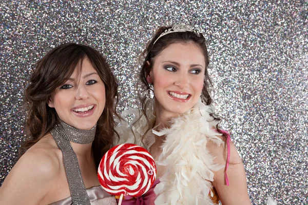 Zwei junge Frauen feiern vor silbernem Hintergrund und essen Bonbons. — Stockfoto