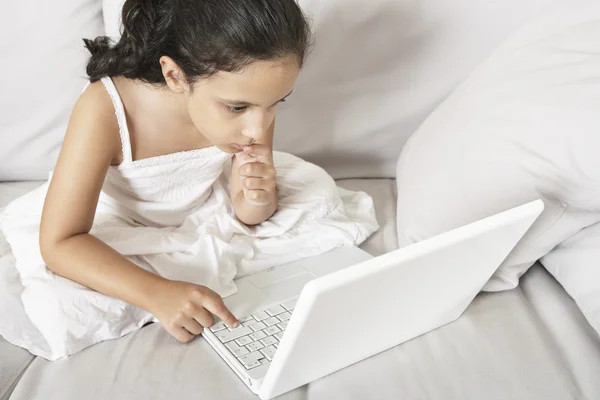 Young girl using a laptop computer while sitting on a white sofa at home. — Stock Photo, Image