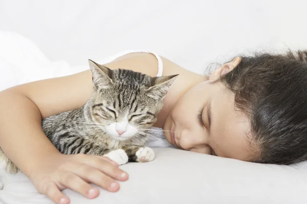 Ung flicka och kattunge sover på en vit soffa hemma. — Stockfoto