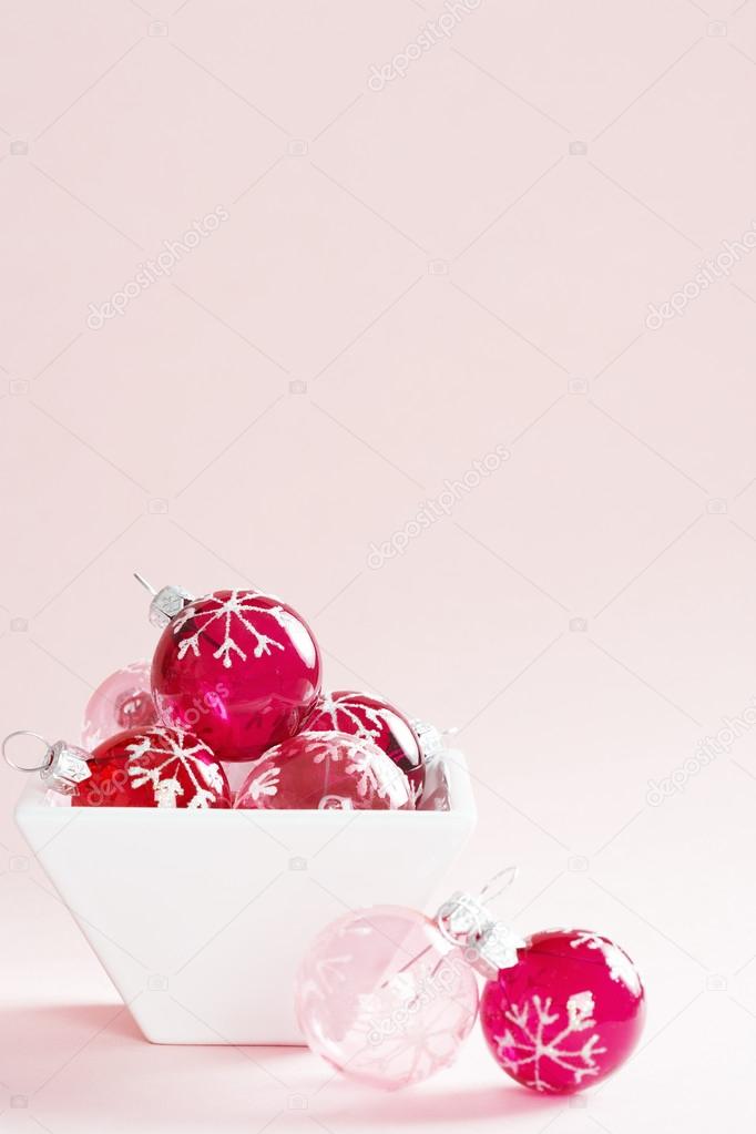 Small Christmass balls in a small container on a pink background.
