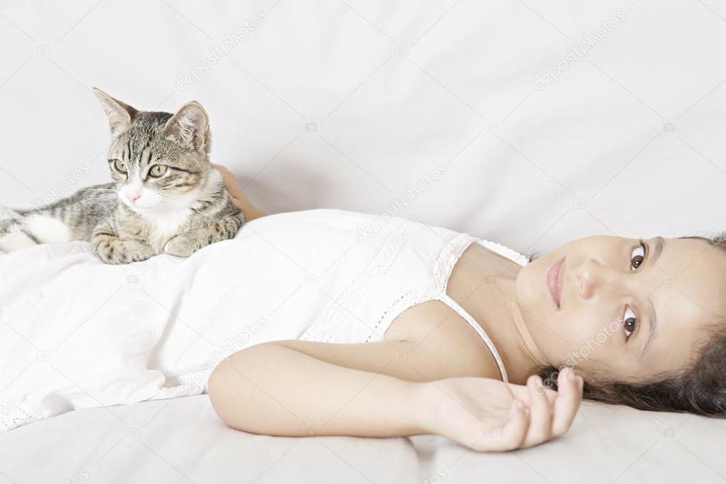 Young girl and kitten laying down on a white sofa.
