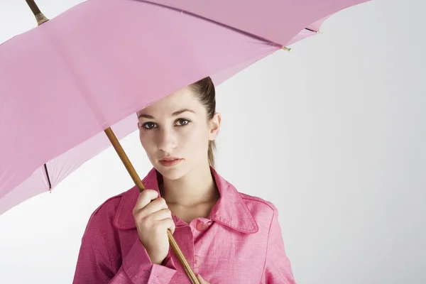 Young woman under a large pink umbrella on a plain background. — Stock Photo, Image