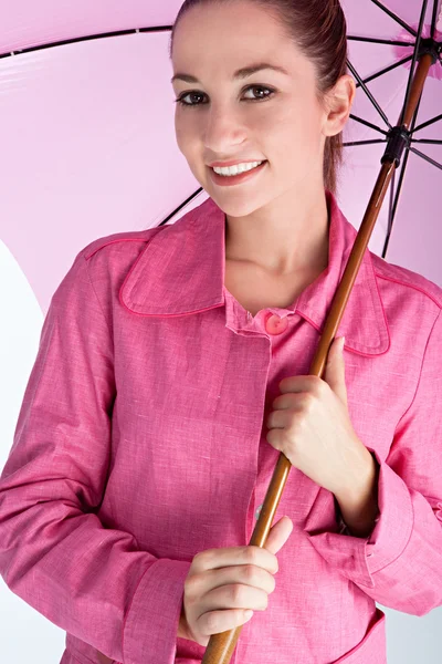 Привлекательная молодая женщина под ярко-розовым зонтом в розовом дождевом пальто — стоковое фото