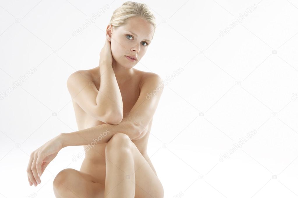 Young nude woman sitting down on a white background looking at camera.