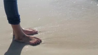 kadının ayakları ile gelen dalgalar kıyıya 's kuma batıyor.