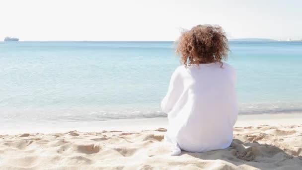 Powrót widok młoda dziewczyna siadając przy brzegu morza, patrząc na horyzoncie. — Wideo stockowe