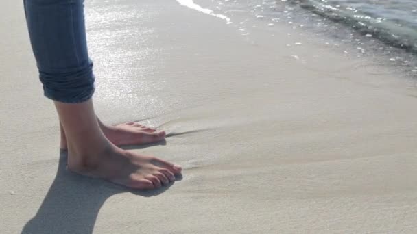 Pies de mujer hundiéndose en la arena de la orilla con olas entrando . — Vídeos de Stock