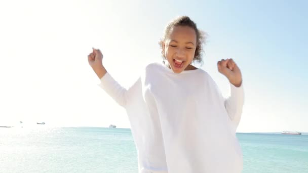 Meisje dansen en zingen op een strand met de blauwe zee en hemel op de achtergrond. — Stockvideo