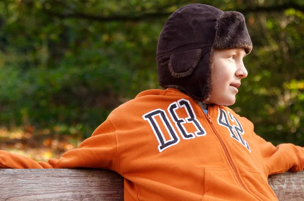 Jongen zittend op een bankje in een park — Stockfoto