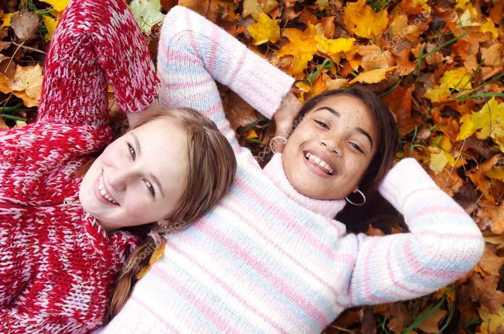 Two young girls laying on autumn leaves