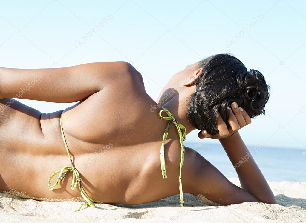 beautiful young woman in black bikini laying in the sunshine on the beach  in the sand - a Royalty Free Stock Photo from Photocase