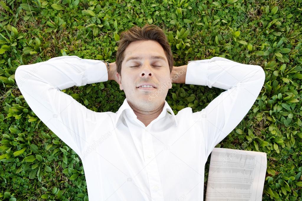 Businessman laying down on green grass