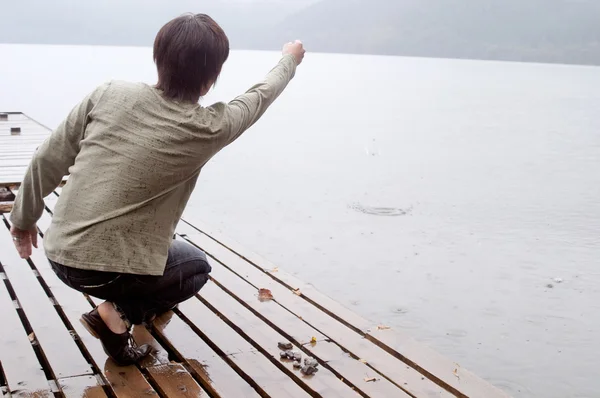 Man crouching on the pier of a lake — Stock Photo, Image