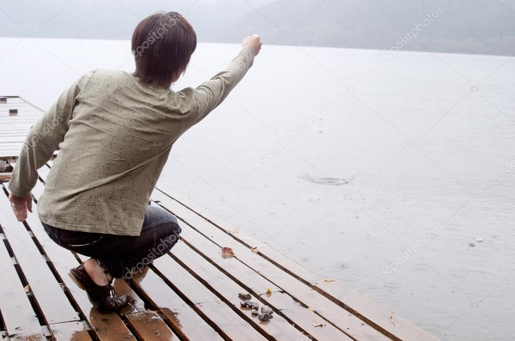 Man crouching on the pier of a lake