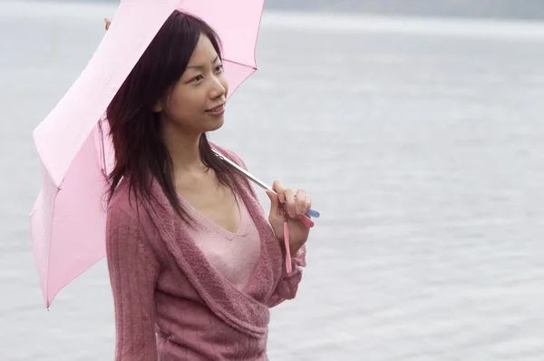 Frau steht an einem See und hält einen rosa Regenschirm in der Hand — Stockfoto