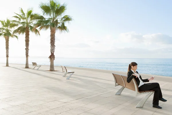 Empresária sentada em um banco de madeira junto ao mar — Fotografia de Stock