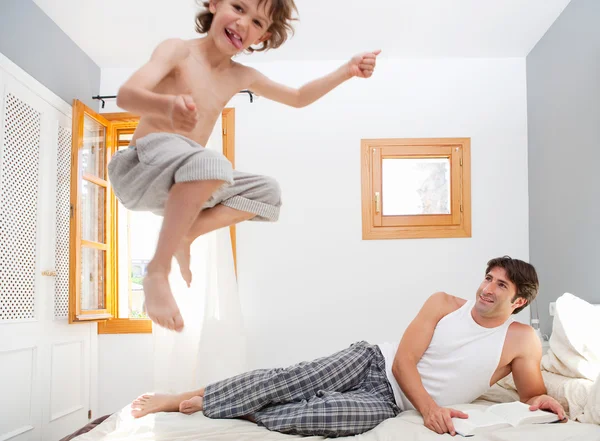 Niño está saltando en la cama cerca de padre —  Fotos de Stock