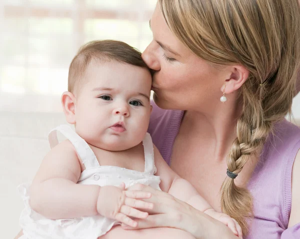 Mãe segurando e beijando seu bebê menina — Fotografia de Stock