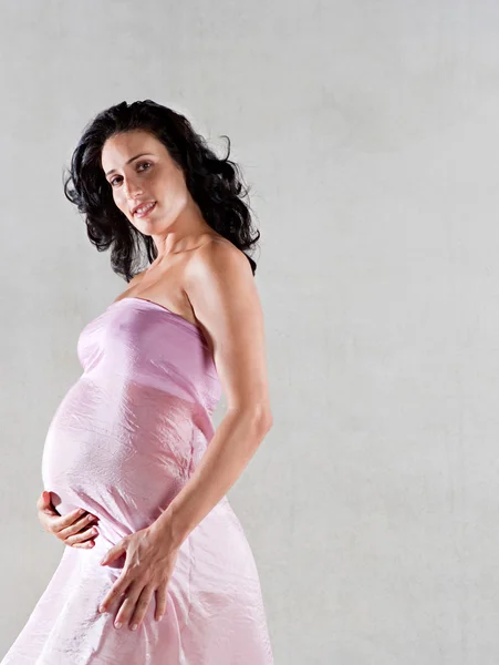 Zwangere vrouw verpakt in roze zijde — Stockfoto