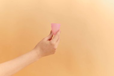 Regl bardağını renkli arka planda tutan kadına yakın durun. Kadın sağlığı konsepti, sıfır atık alternatif