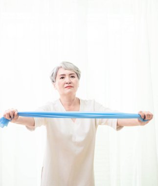 Kıdemli Asyalı kadın evde direniş bandıyla egzersiz yapıyor..