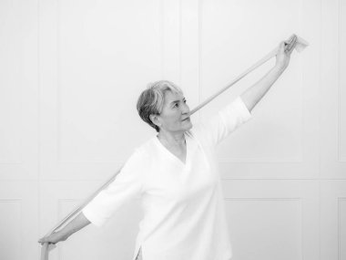 Kıdemli Asyalı kadın evde direniş bandıyla egzersiz yapıyor..